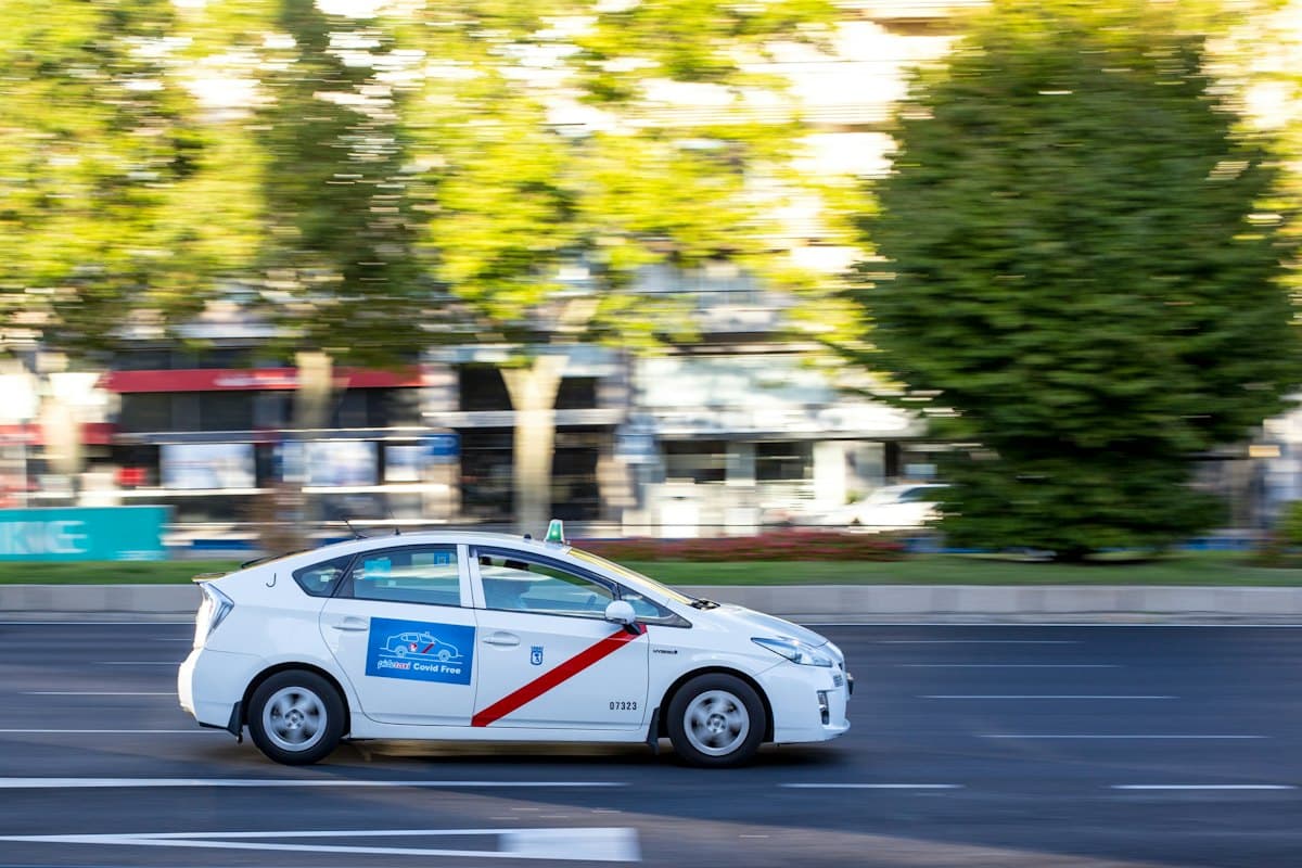 White hybrid sedan driving along a tree-lined city street